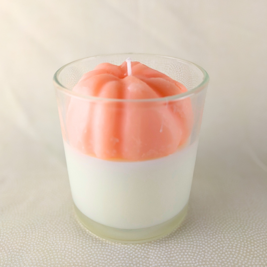 Candle in a glass holder with a pink top and white bottom on a textured surface.