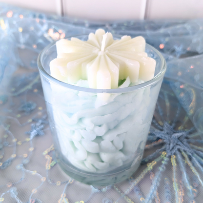 White frosted cookie-shaped candle in a glass container on a decorative blue surface