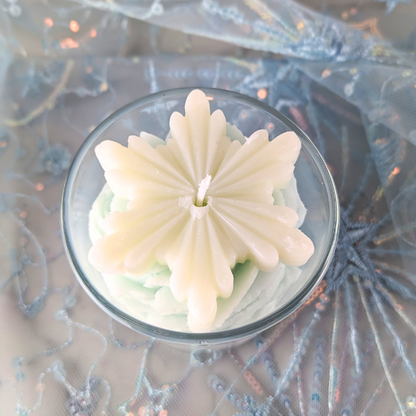 Decorative candle with a floral design in a glass container on a textured background.
