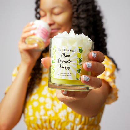 Person holding a candle jar with a label, wearing a yellow dress.