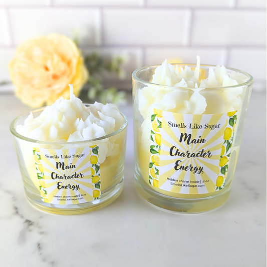Two candles in glass jars with lemon-themed labels on a marble surface.