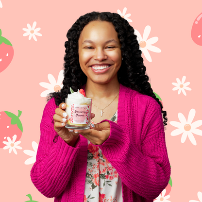 Woman holding a candle with strawberry design against a pink background with floral and strawberry patterns
