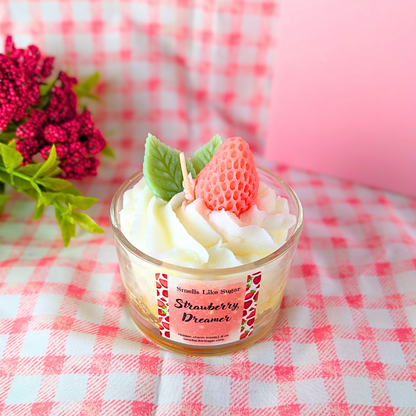 Small glass jar with wax whipped cream, wax strawberry, and wax mint leaves on a pink and white checkered tablecloth.