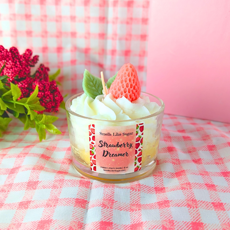 Candle labeled 'Strawberry Dreamer' on a pink checkered tablecloth with flowers in the background.