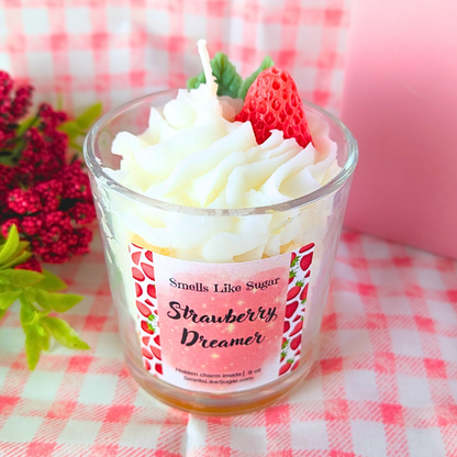 Strawberry-themed candle with whipped cream and a strawberry on top, placed on a checkered tablecloth.