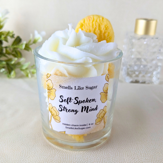 Candle with a label reading 'Smells Like Sugar Soft Spoken, Strong Mind' on a light background.