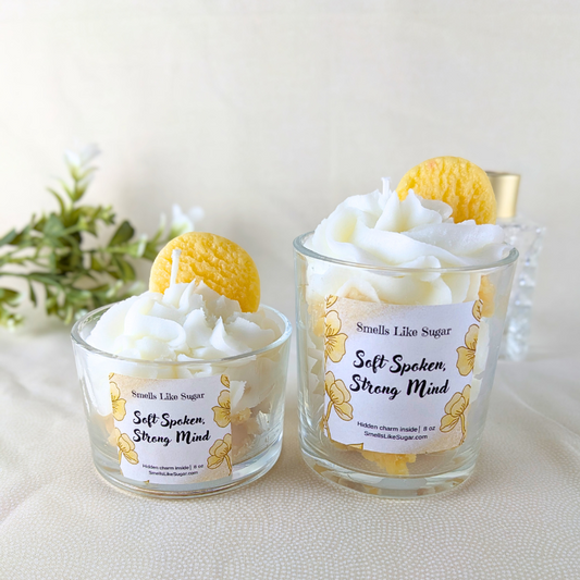 Two glass containers with whipped cream wax and wax cookies on a white surface with a plant in the background.